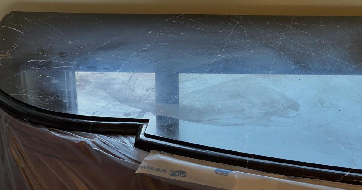 Curved edge of a dark polished stone worktop with protective tape